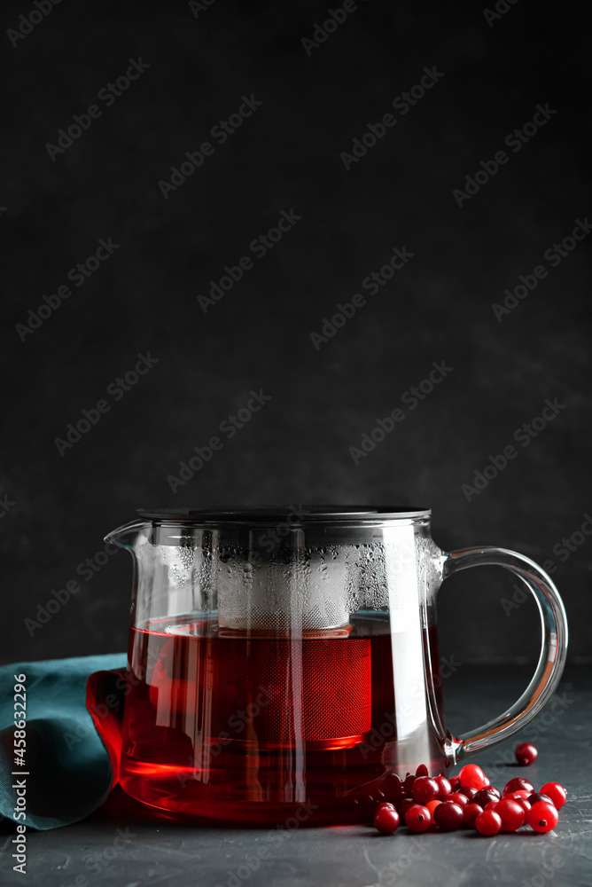 Teapot of tasty tea with cranberry on dark background