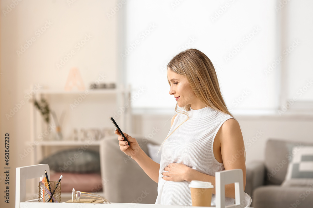 怀孕的女商人在家使用手机