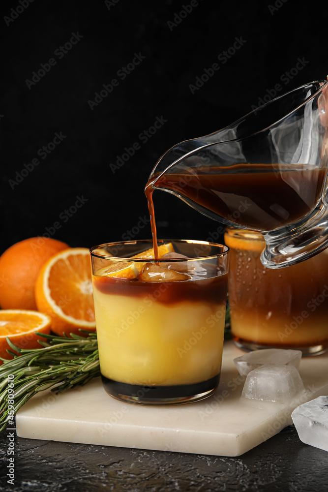 将壶中的咖啡倒入深色背景的橙汁玻璃杯中