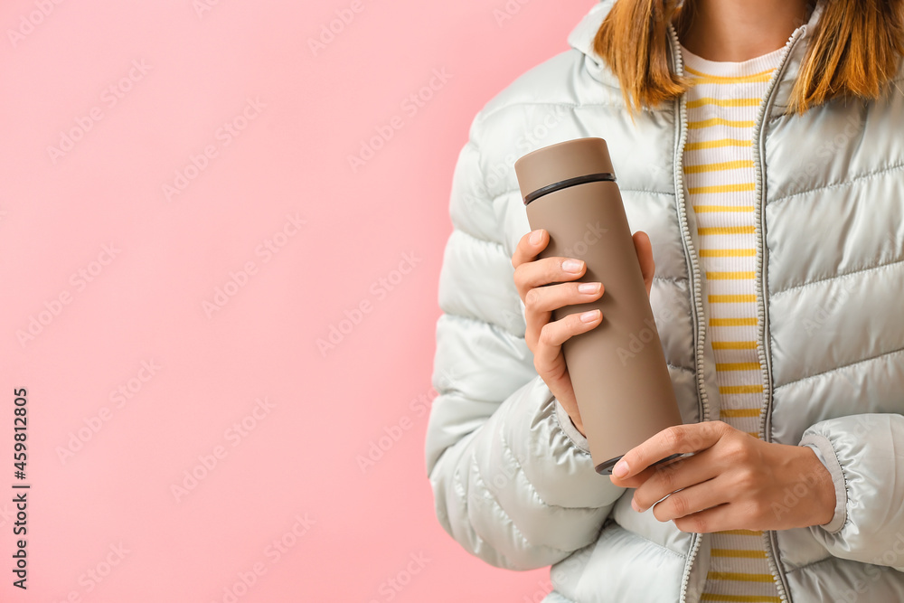 Young woman in warm clothes and with thermos on color background