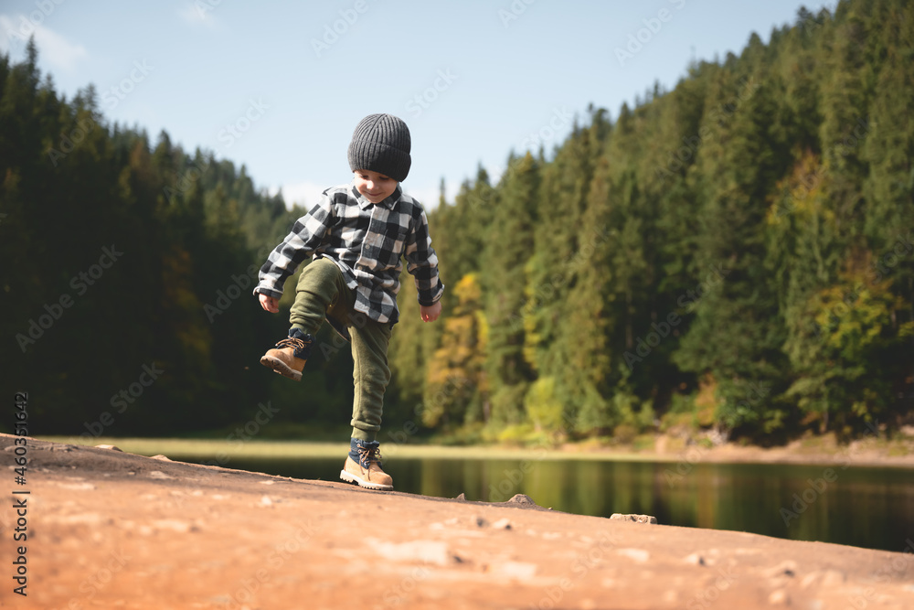 在森林湖泊海岸，穿着格子衬衫和灰色帽子的小男孩。童年与热爱自然的人在一起