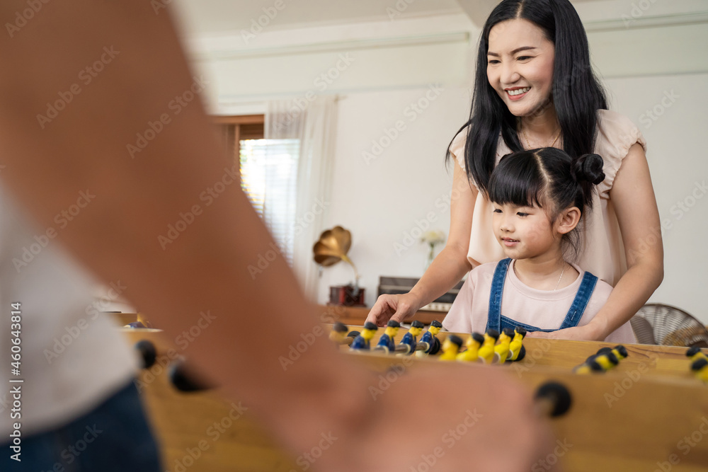 亚洲小女儿和父母一起踢桌上足球或足球比赛。