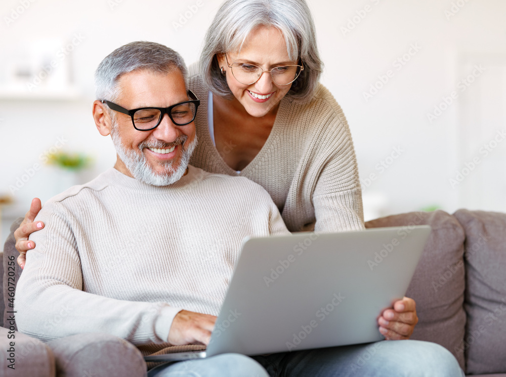 快乐的老年家庭夫妇在家空闲时间用笔记本电脑看喜剧或搞笑视频
