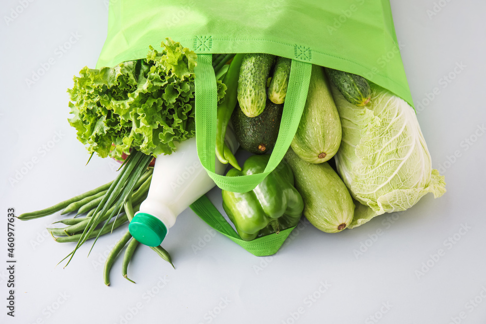 环保袋，浅色背景下有蔬菜、绿色蔬菜和一瓶牛奶，特写