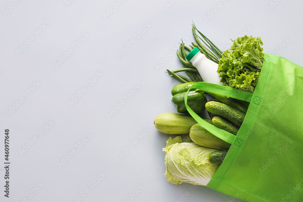浅色背景的环保袋，里面有蔬菜、绿色蔬菜和一瓶牛奶