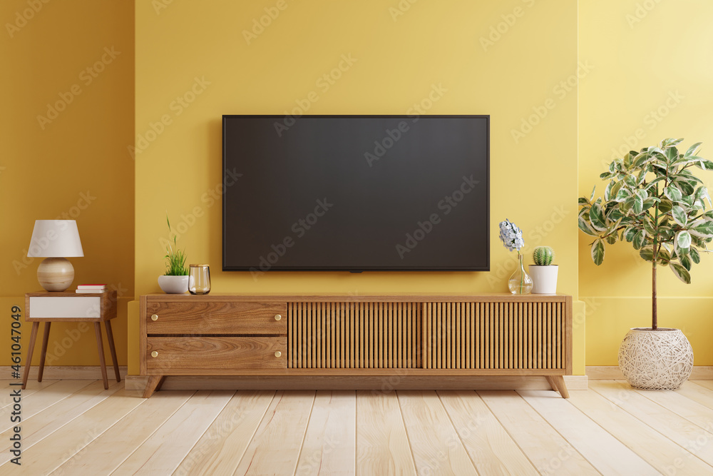 黄色的墙壁背景，电视安装在现代客厅的木橱柜上。