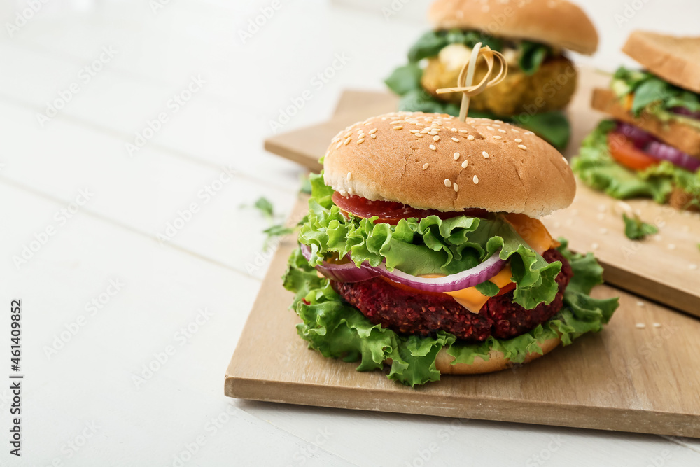 Wooden boards with tasty vegetarian burgers on white wooden background