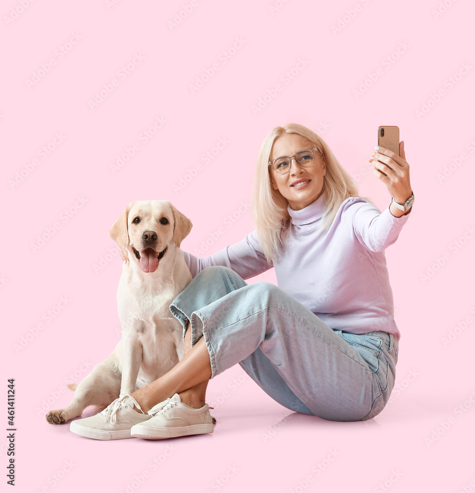 成熟的女人和可爱的拉布拉多犬在粉色背景下自拍
