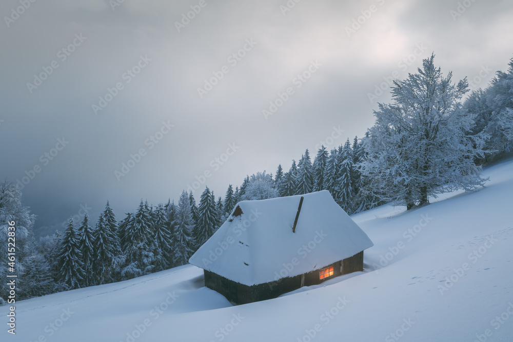 梦幻般的冬季景观，在白雪皑皑的森林中有发光的木屋。喀尔巴阡山脉的舒适房子