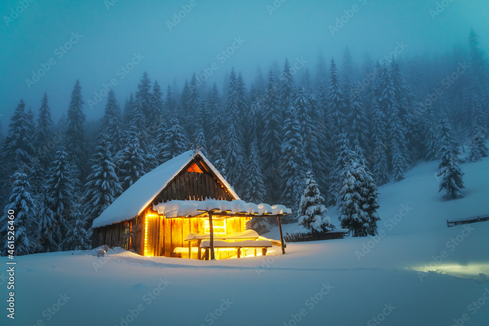 Fantastic winter landscape with glowing wooden cabin in snowy forest. Cozy house in Carpathian mount