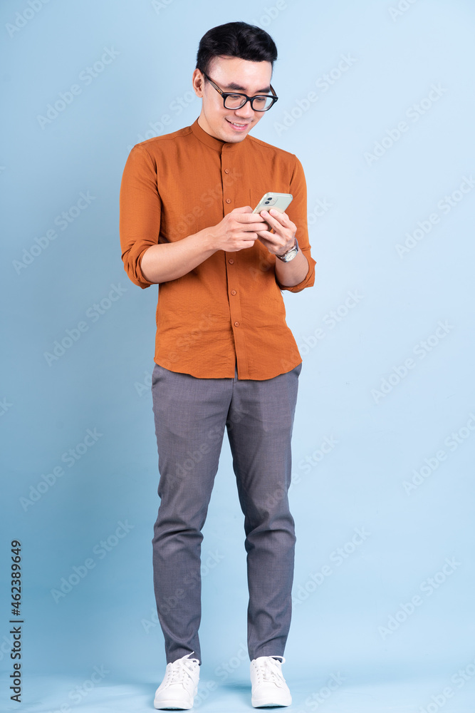 年轻的亚洲男子在蓝色背景下使用智能手机