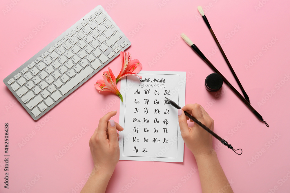 用画笔在粉色背景上书写字母表的女人
