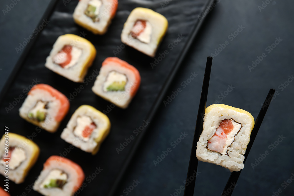 深色背景下的筷子配美味的寿司卷