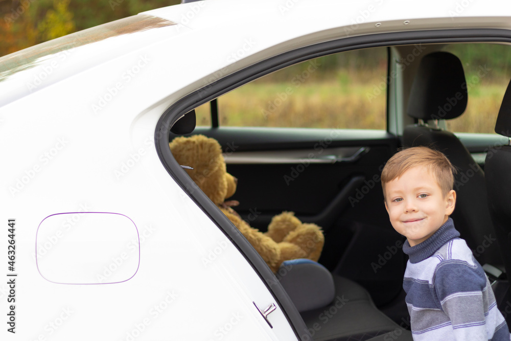 一个温暖晴朗的秋日，一个七岁的可爱男孩带着一只玩具熊在汽车沙龙里。选择性聚焦。