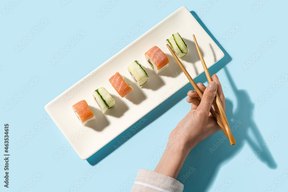 女人从盘子里拿寿司卷，背景是彩色的