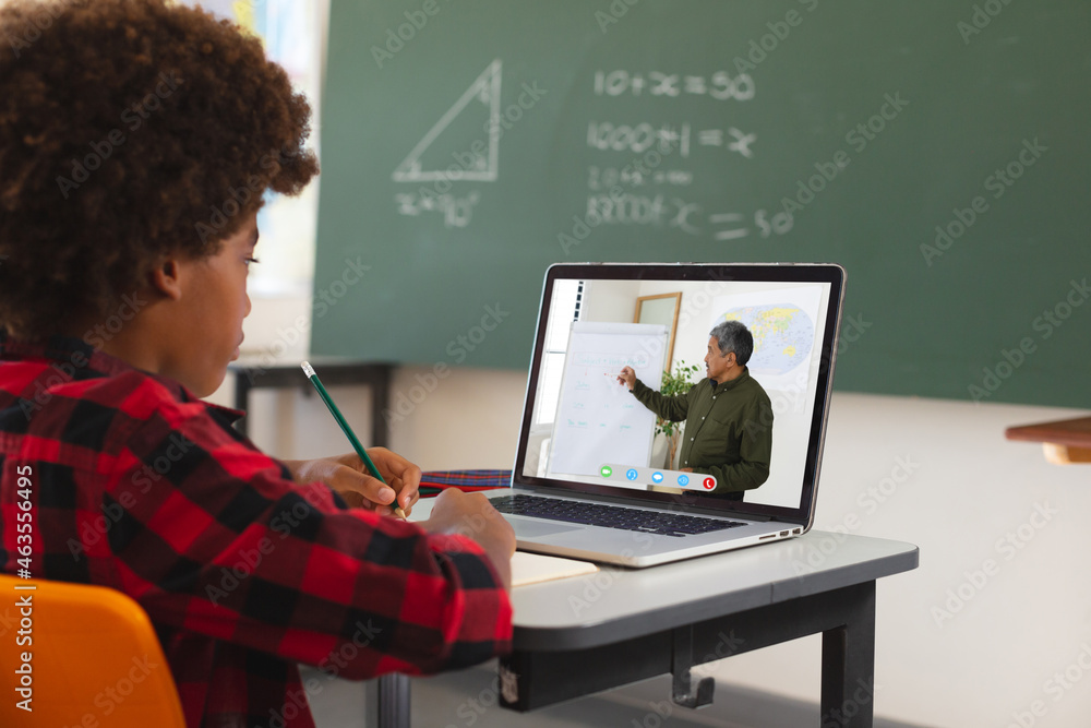 African american boy using laptop for video call, with male teacher on screen