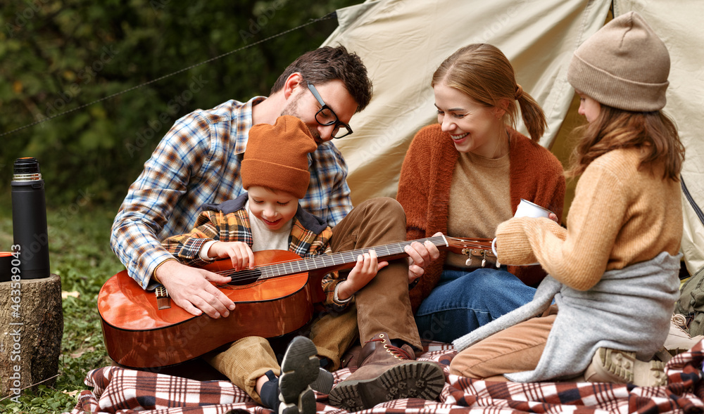 父亲、母亲和小儿子在露营时坐在旅游帐篷附近弹吉他