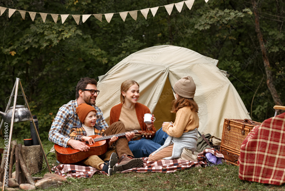 爸爸、妈妈和小儿子在露营时坐在旅游帐篷附近弹吉他