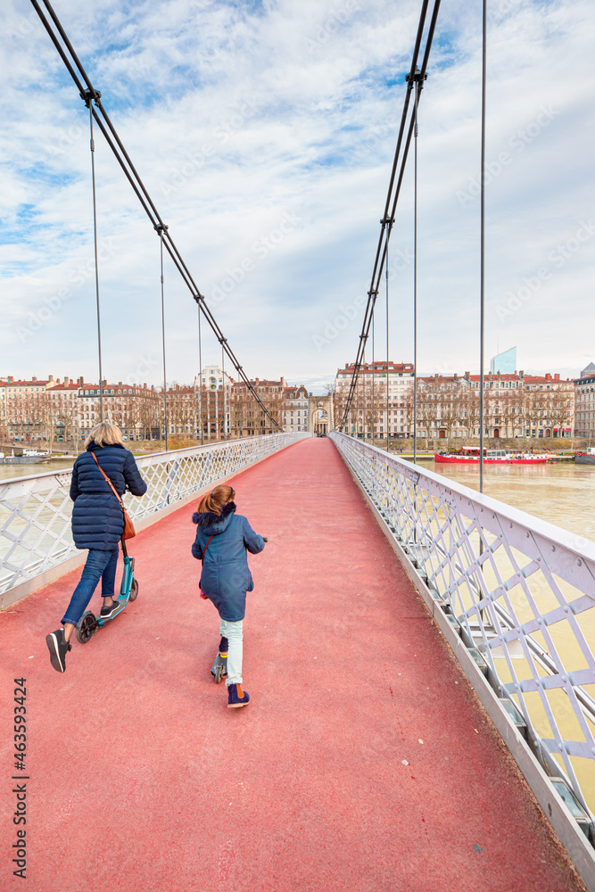 Mother and her daugter riding scooters on the Old Passerelle du College bridge - Lyon, France