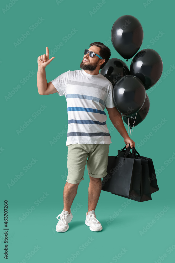 黑色星期五购物袋和绿色背景气球的英俊男人
