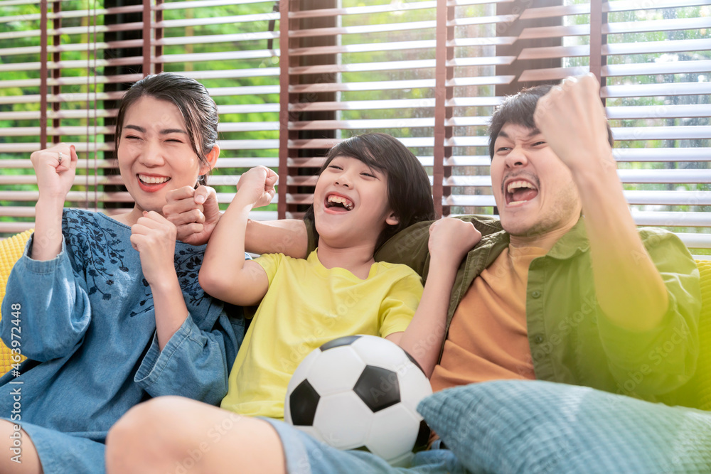 Exited Cheerful Joyful Asian parents And Son Watching Sports On TV Cheering Favorite Soccer Team, Si