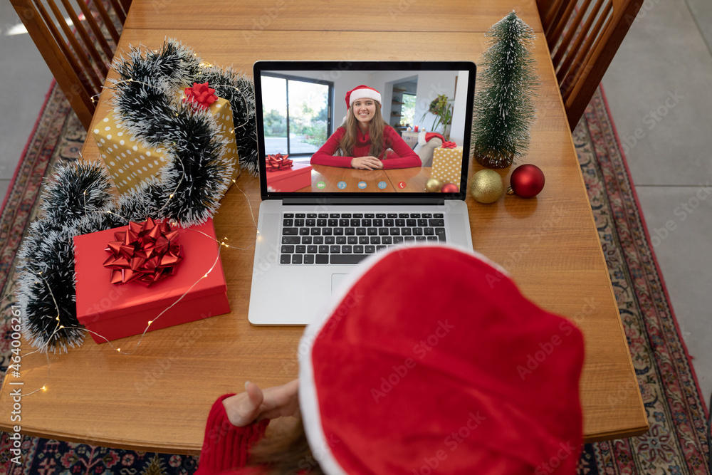 戴圣诞老人帽的白人妇女在圣诞笔记本电脑上与女性朋友视频通话