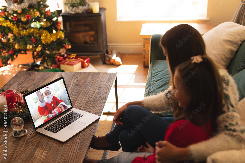 Caucasian mother and daughter in santa hat on christmas laptop video call with santa claus