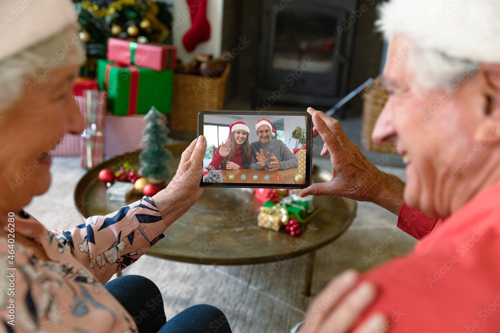 快乐的高加索老年夫妇与微笑的父女进行平板电脑圣诞视频通话