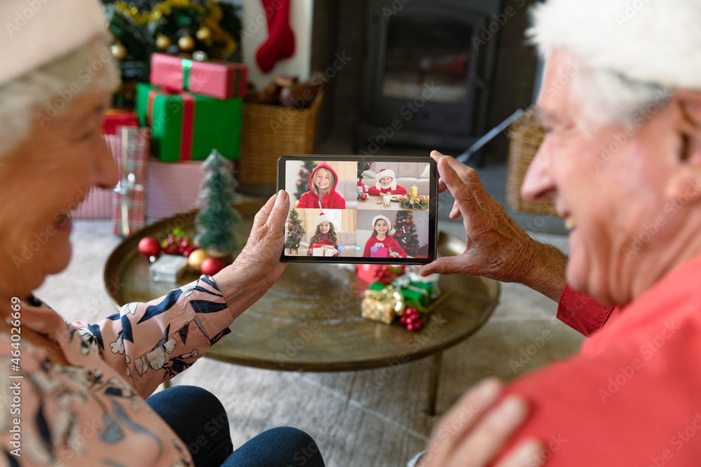 快乐的高加索老年夫妇与四个微笑的孙女进行平板电脑圣诞视频通话