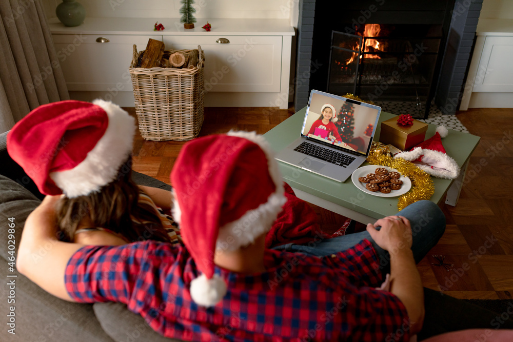 Caucasian couple in santa hats on christmas video call on laptop with caucasian girl