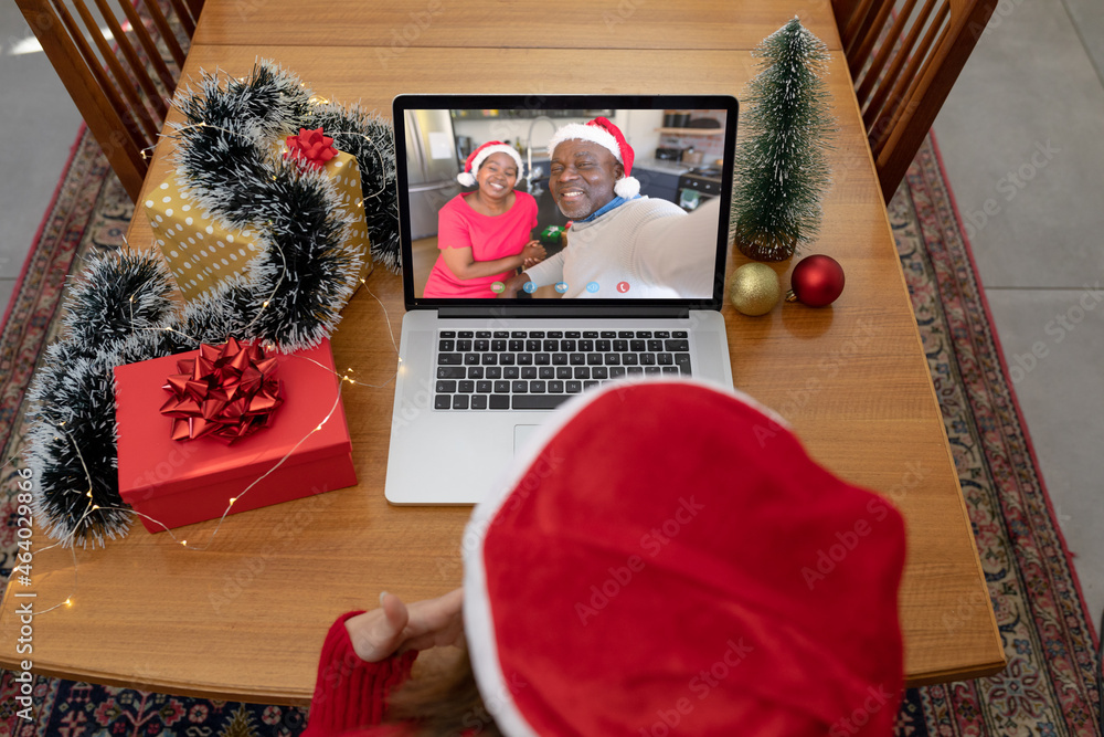 戴圣诞老人帽的白人妇女与非裔美国人朋友在笔记本电脑上视频通话