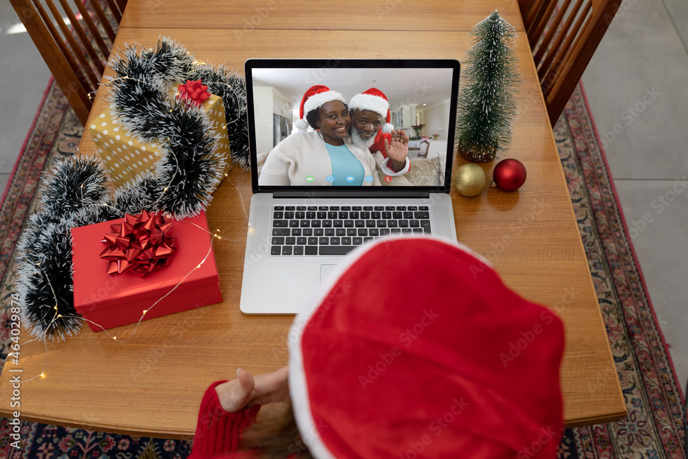 Caucasian woman in santa hat on christmas video call on laptop with african american friends