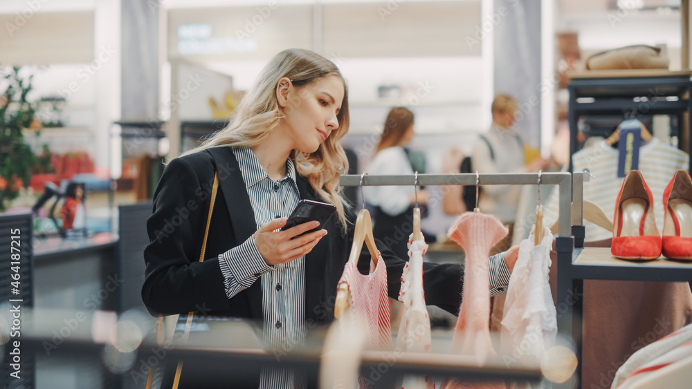美丽微笑的女顾客在服装店购物，使用智能手机，在线浏览，Com