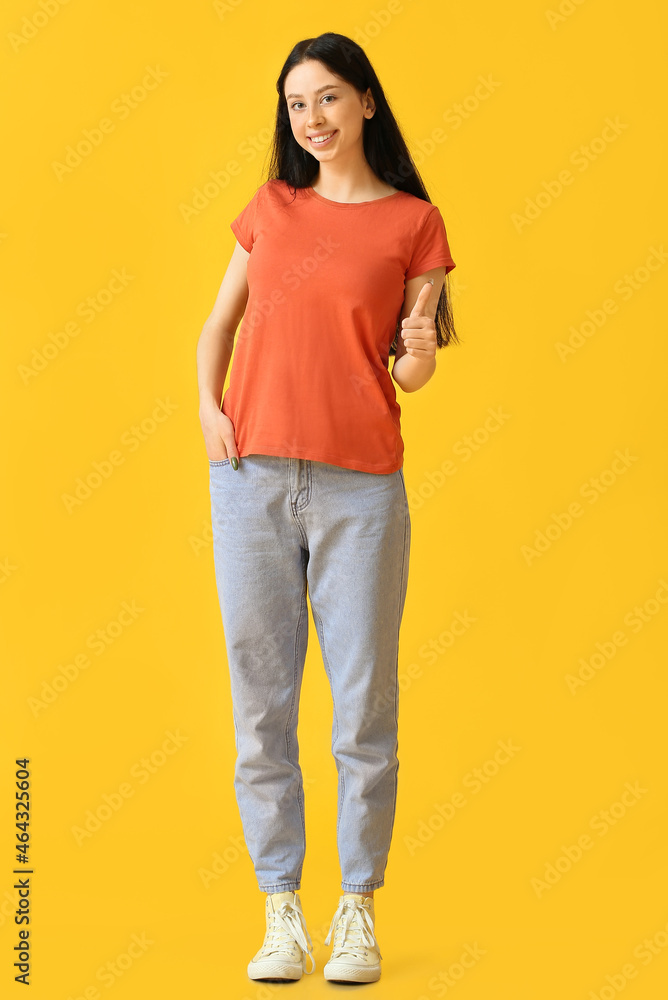 穿着橙色t恤的漂亮少女在黄色背景上竖起大拇指