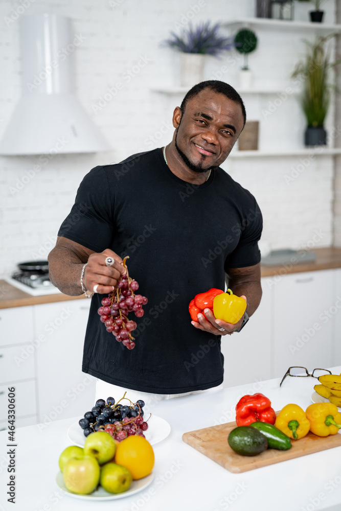 厨房里的多种族男子准备用蔬菜和水果做饭。男子拿着葡萄。