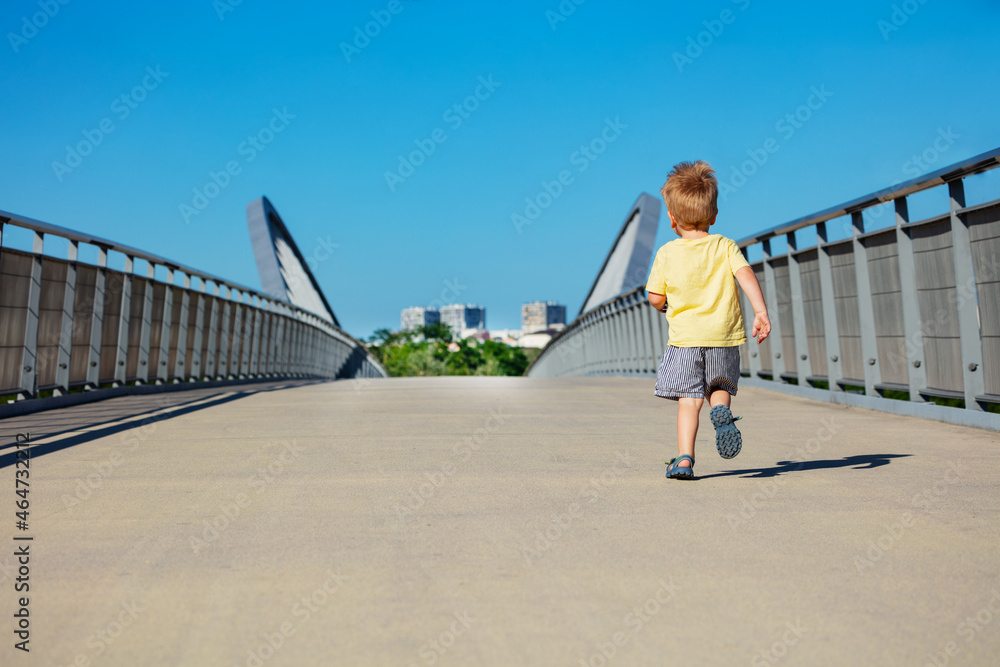 金发蹒跚学步的男孩在公园的小路上逃跑
