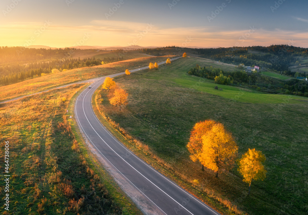 Aerial view of road, hills, green meadows and colorful trees at sunset in autumn. Top view of mounta