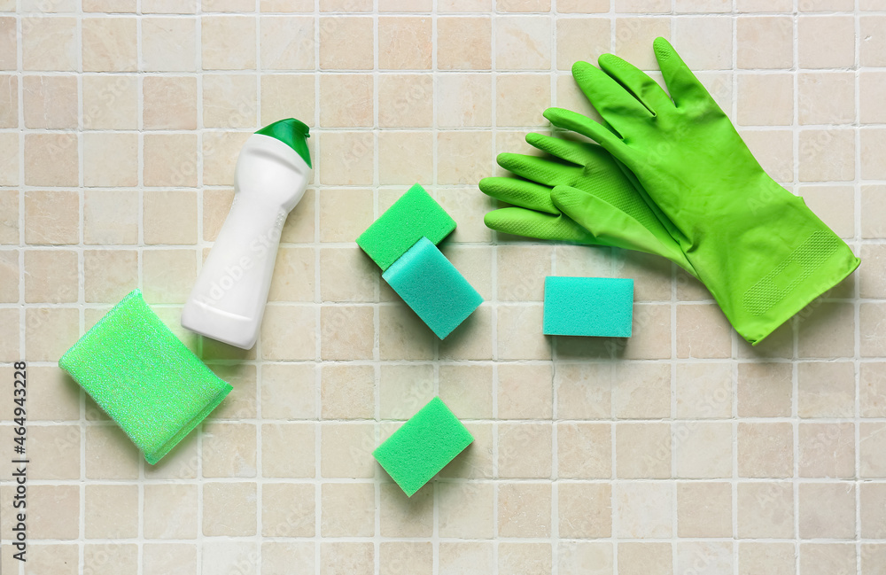 瓷砖背景上的绿色清洁海绵、手套和一瓶洗涤剂