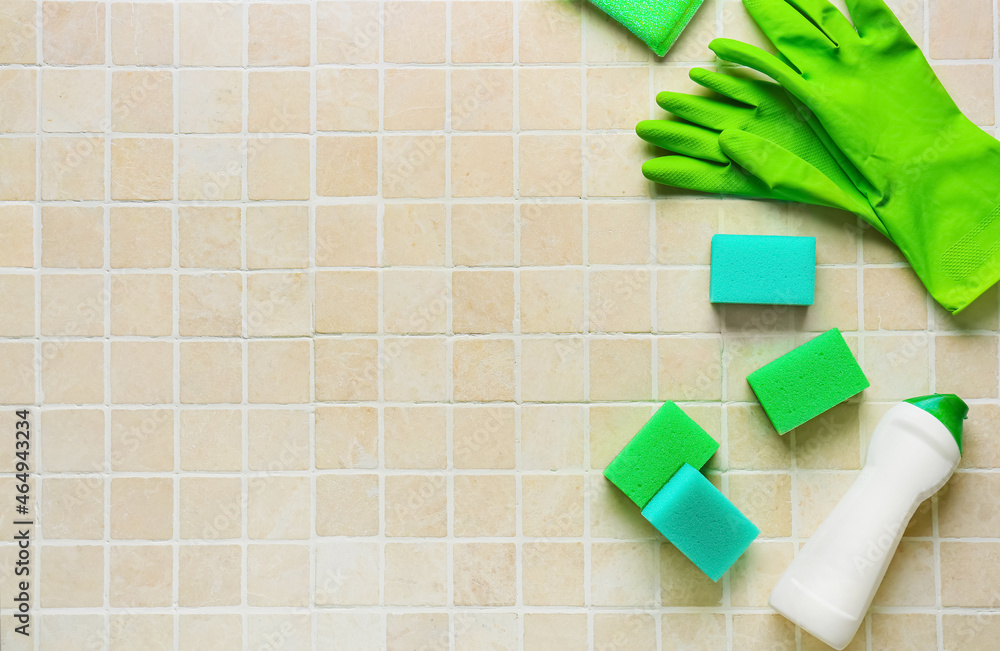 瓷砖背景上的绿色清洁海绵、手套和一瓶洗涤剂