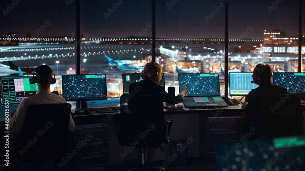 多样化的空中交通管制团队晚上在现代机场塔台工作。办公室里摆满了桌子