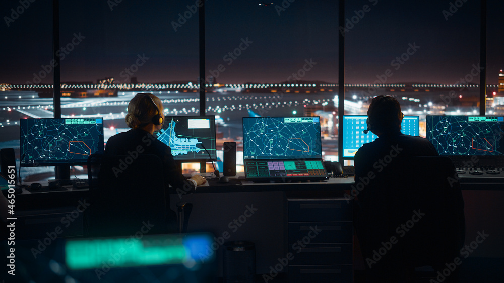多样化的空中交通管制团队晚上在现代机场塔台工作。办公室里挤满了人
