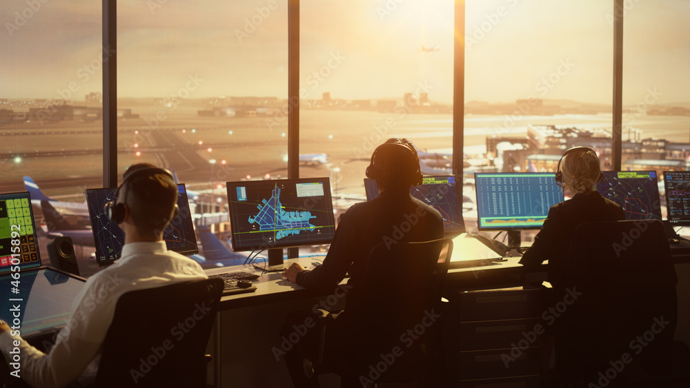多样化的空中交通管制团队在日落的现代机场大楼工作。办公室里摆满了桌子