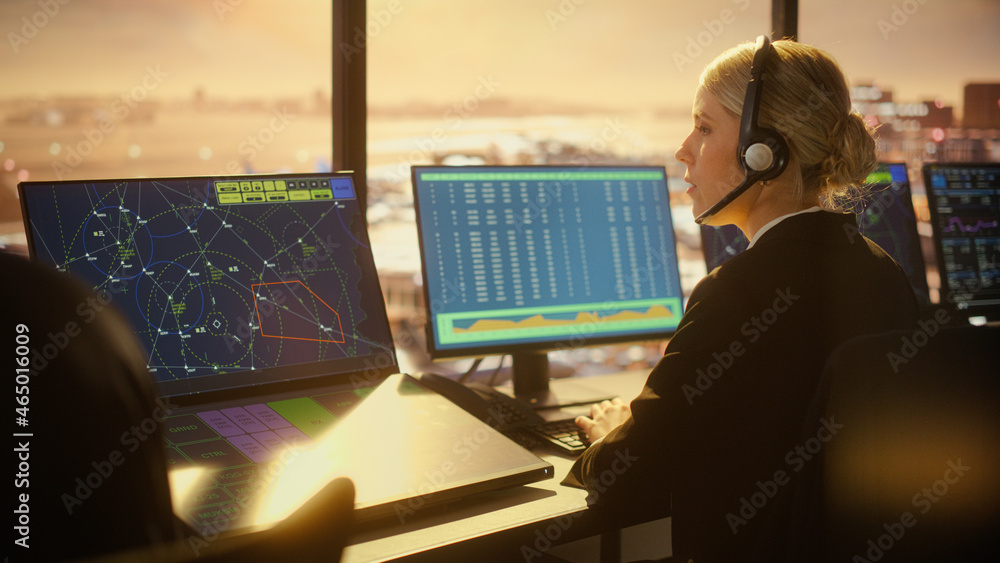 戴耳机的女空中交通管制员在机场塔台讲话。办公室里摆满了台式电脑
