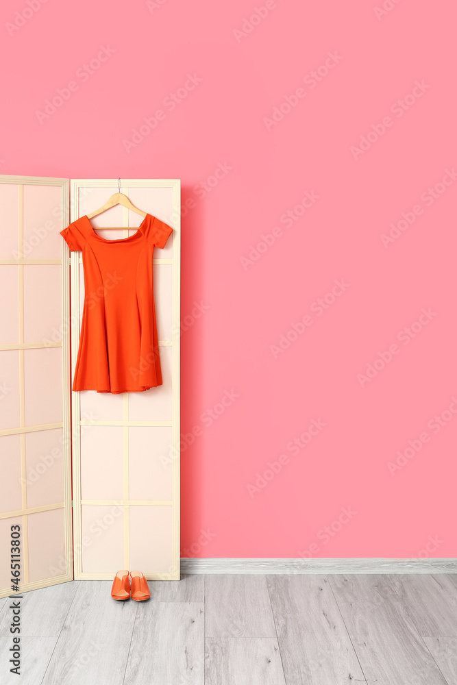 粉色墙壁附近有红色连衣裙和鞋子的轻型折叠屏幕