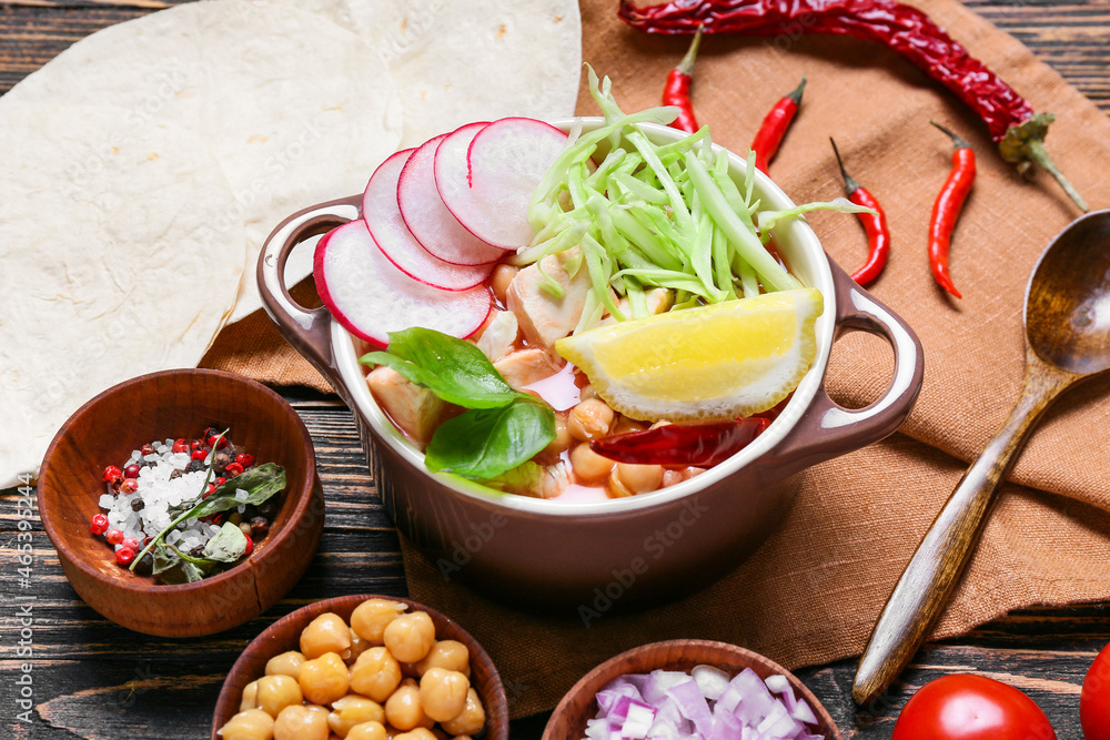 Pot with tasty pozole soup and ingredients on wooden background