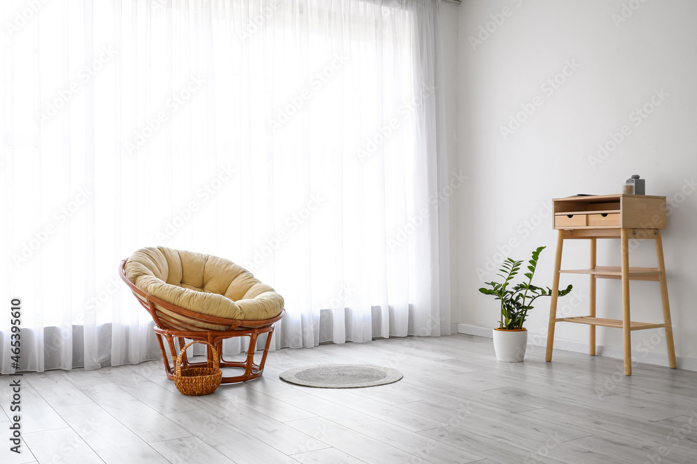 Armchair, stand-up table and houseplant near big window with light curtains