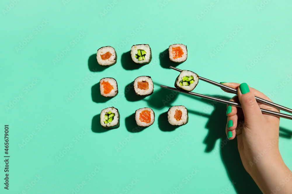 Woman taking maki roll with chopsticks on color background