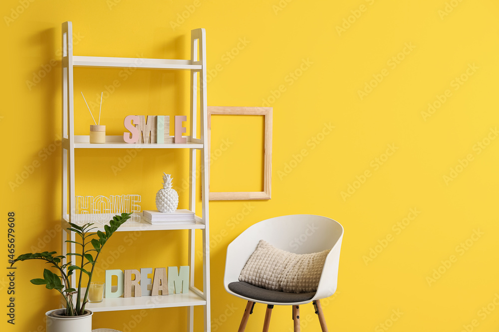 时尚的架子单元，靠近黄色墙壁，配有装饰、室内植物和椅子，特写