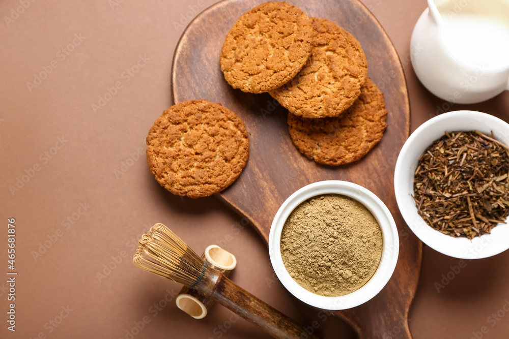 Wooden board with tasty hojicha cookies, powder and chasen on brown background
