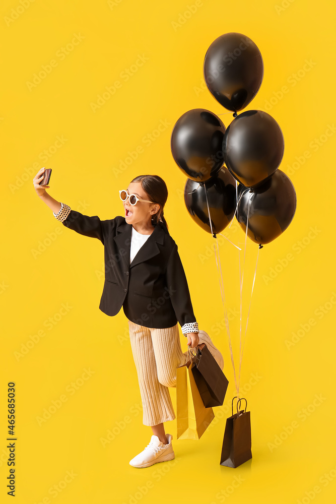 带着黑色星期五购物袋和气球的小女孩在黄色背景下自拍